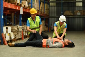 Warehouse staff giving emergency first aid training at work to injured worker
